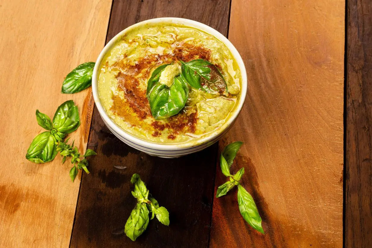 Creamy basil hummus in bowl with olive oil drizzle, fresh basil leaves, and paprika on rustic wood