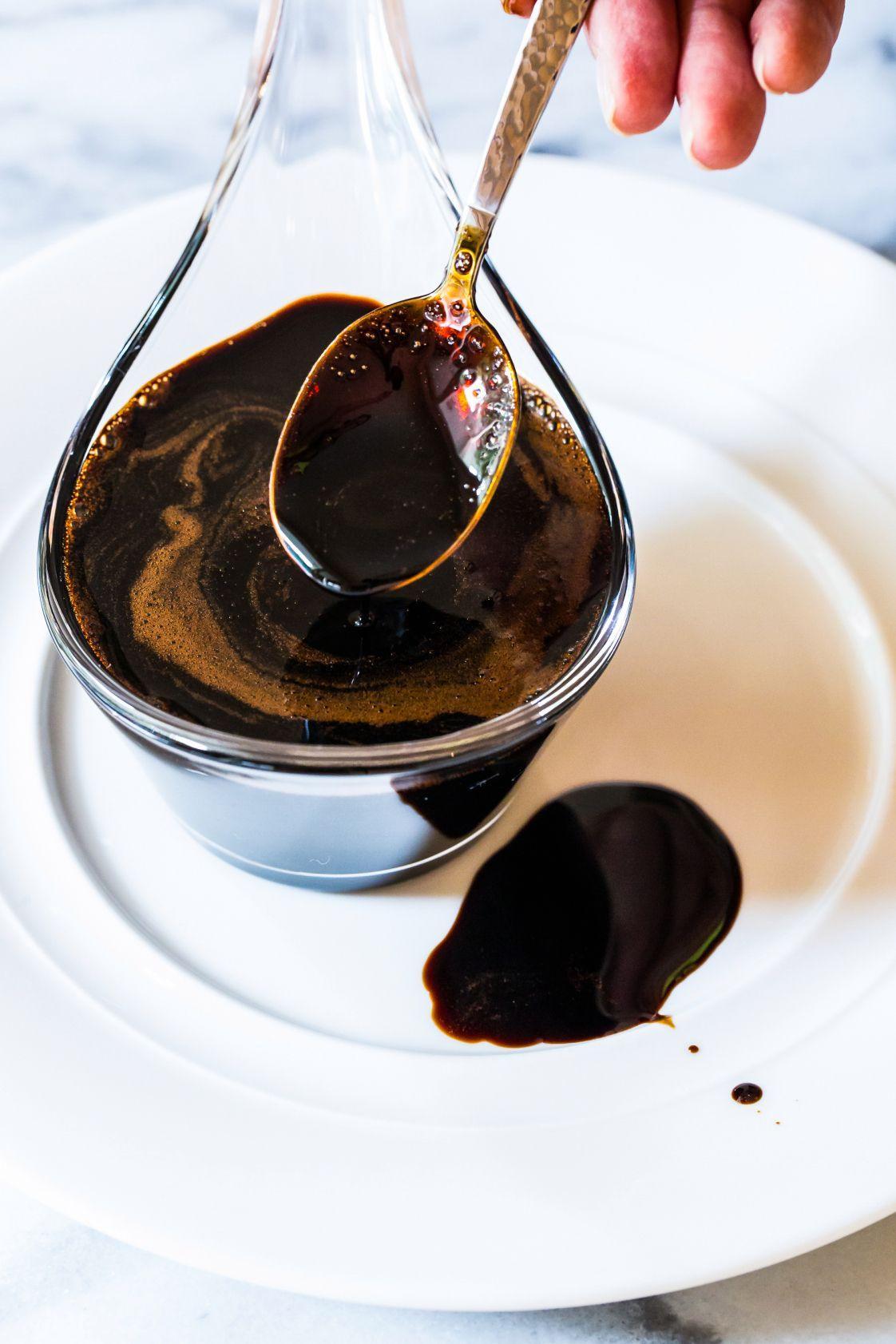 Rich balsamic vinegar drizzled from spoon over white plate, showcasing artisanal quality for gourmet cooking.