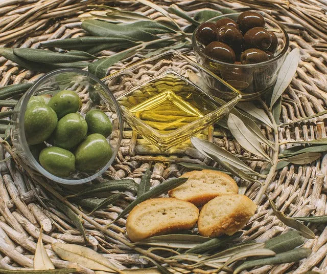 Premium olive oil with green and black olives, fresh leaves, and bread slices on woven mat