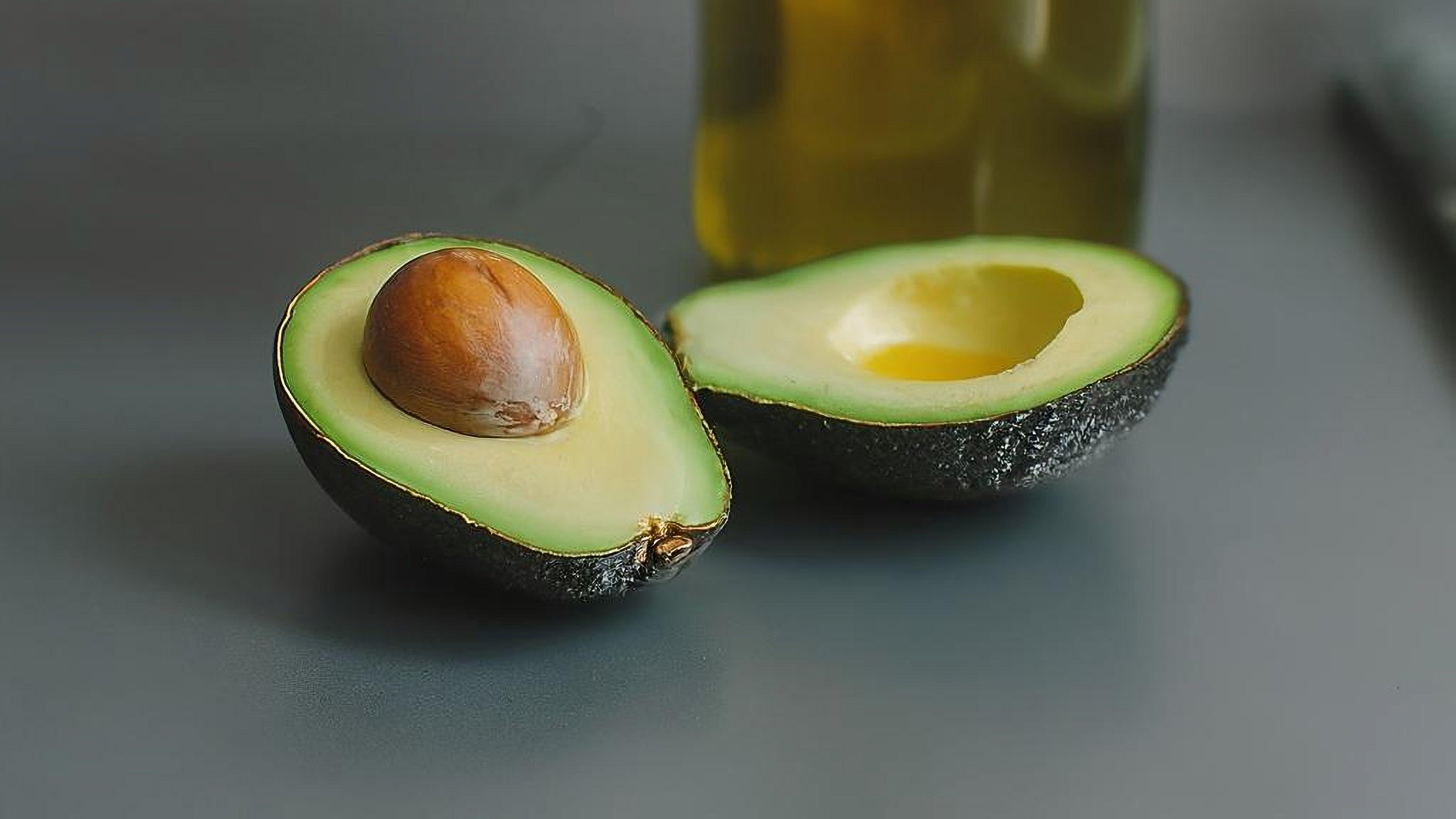 Fresh avocado halves with pit, beside olive oil bottle, showcasing healthy cooking ingredients