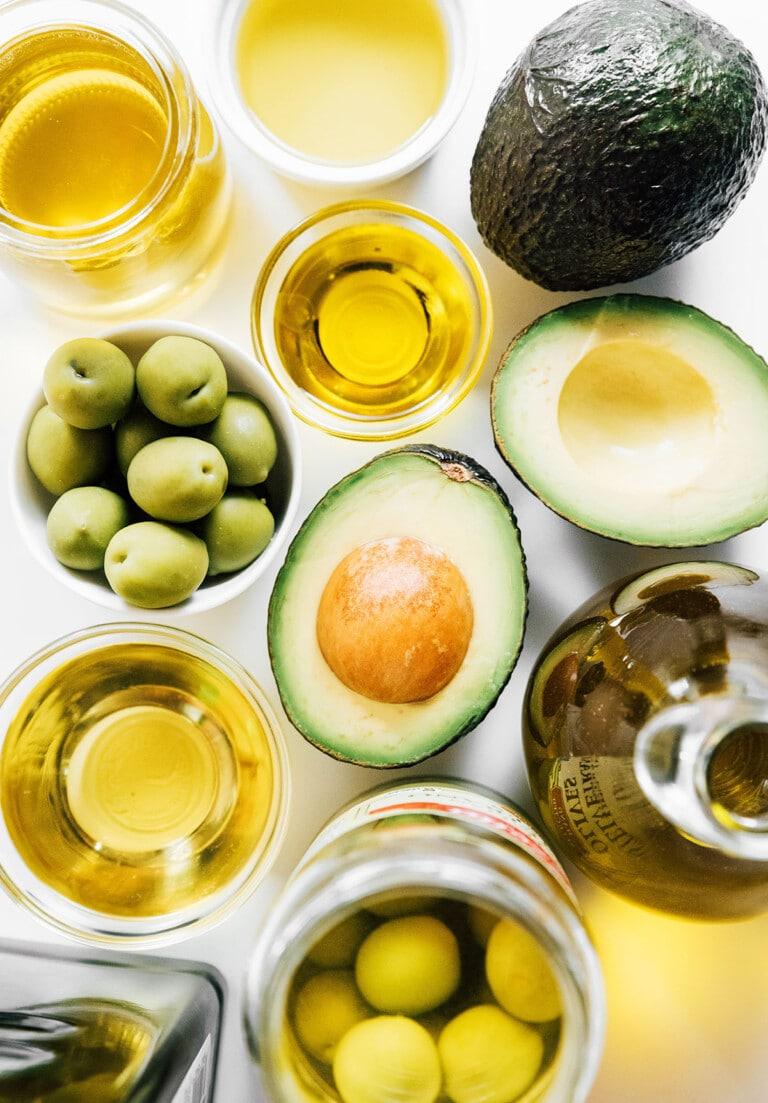 Premium olive oil, green olives, and fresh avocado halves arranged for gourmet cooking