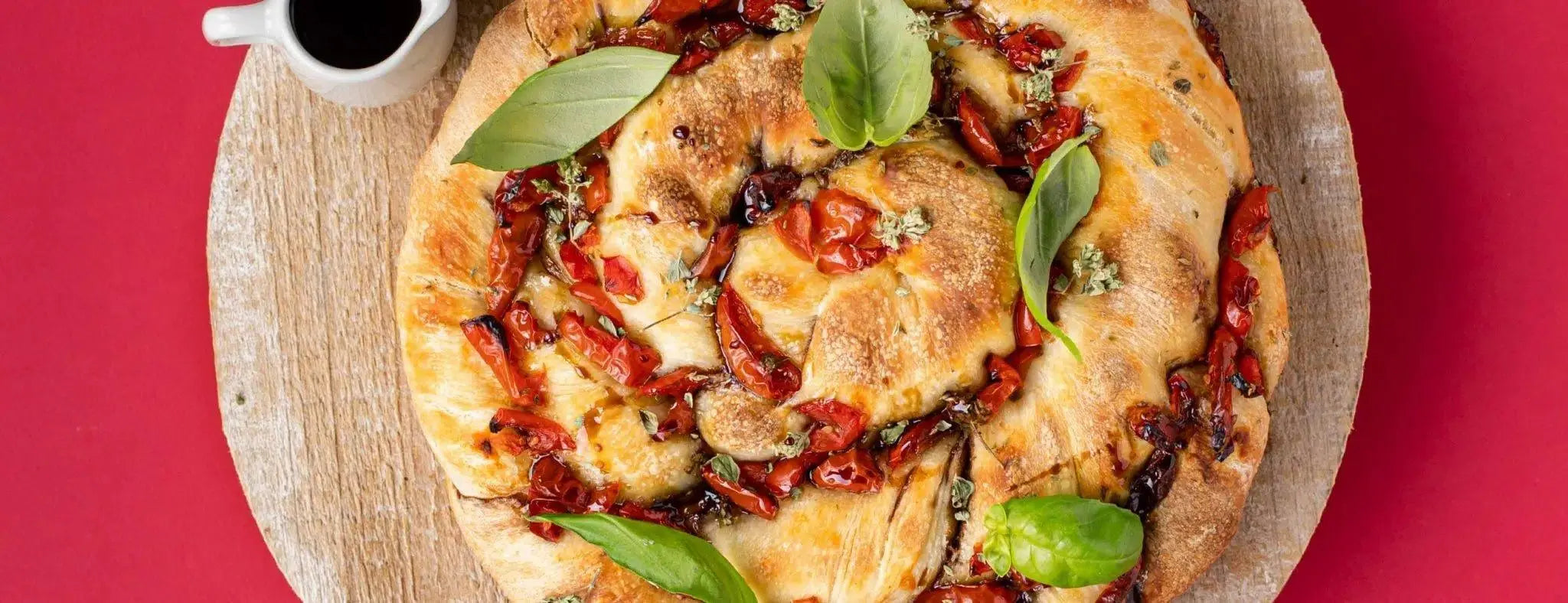 Artisanal focaccia bread with sun-dried tomatoes, fresh basil, and balsamic glaze on wooden board