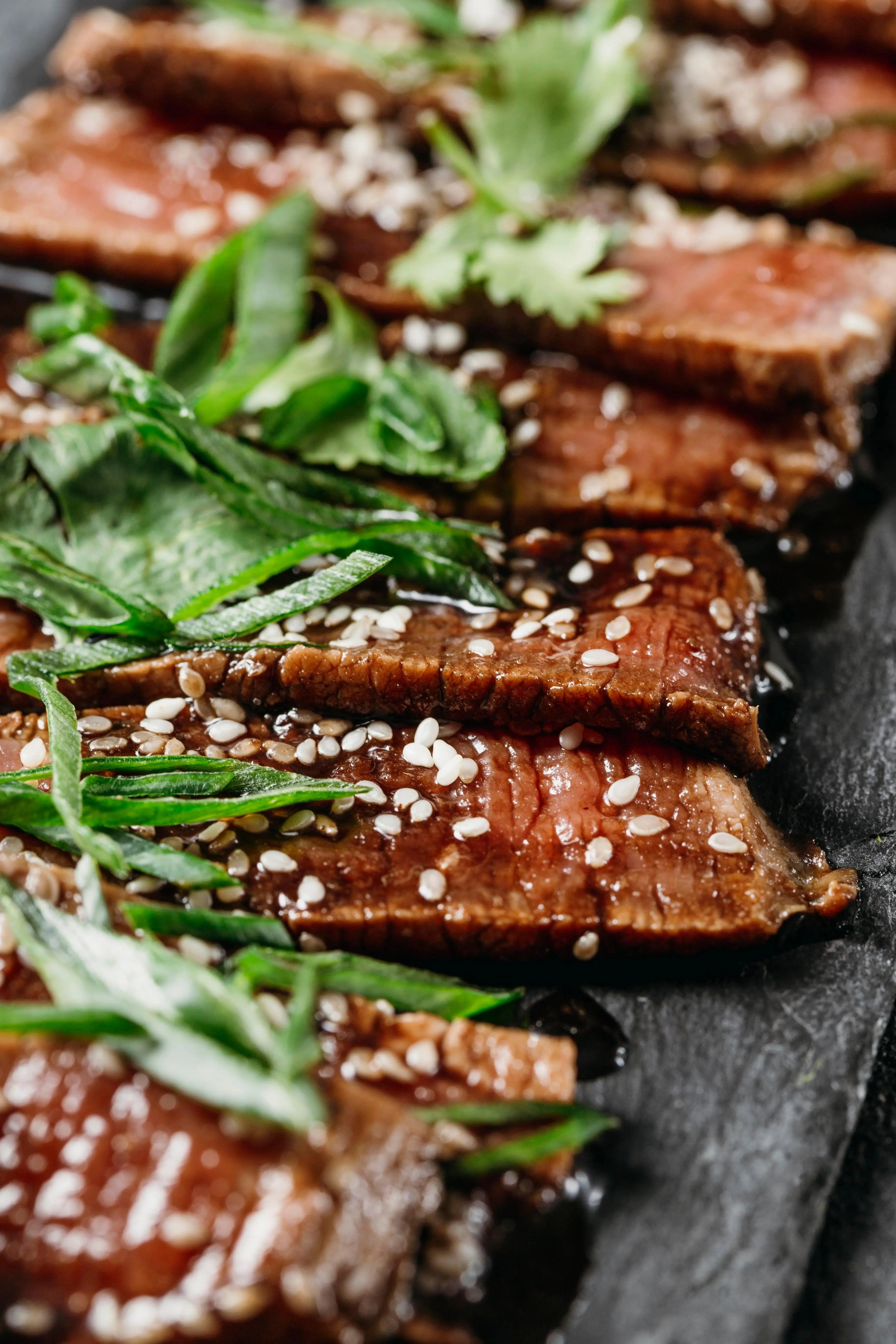 Sliced steak with sesame seeds and fresh herbs, glazed with premium olive oil