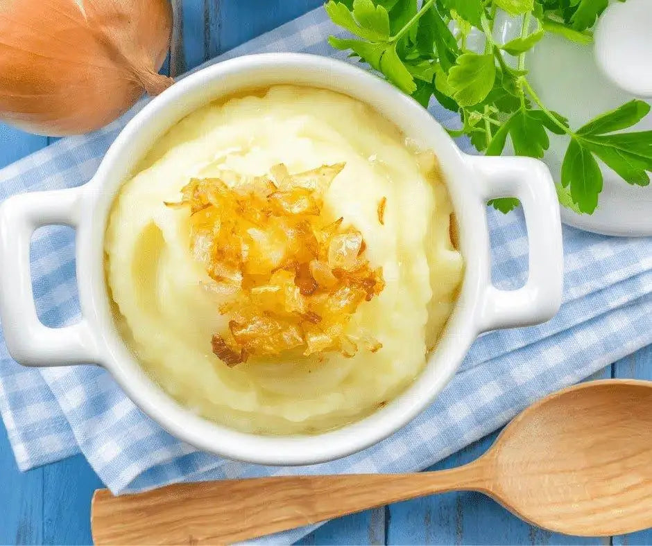 Creamy mashed potatoes topped with caramelized onions, served in white bowl with parsley and wooden spoon