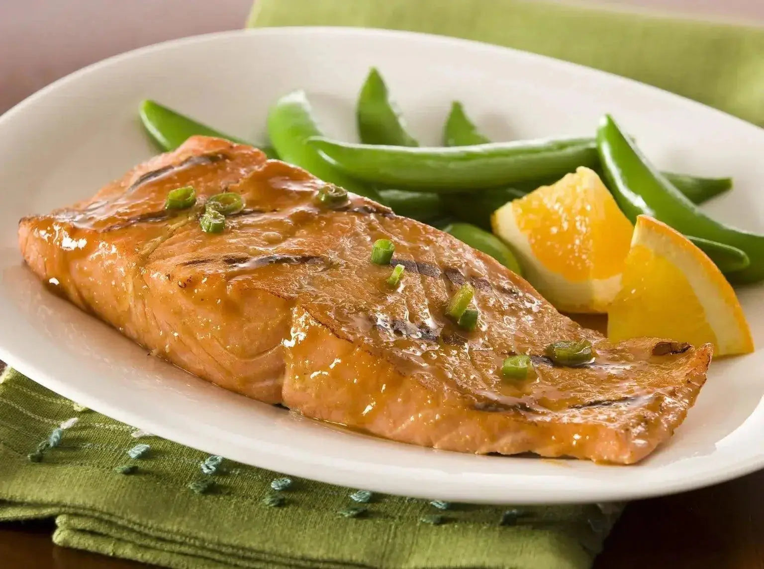 Grilled salmon with orange glaze, snow peas, and green onions on white plate