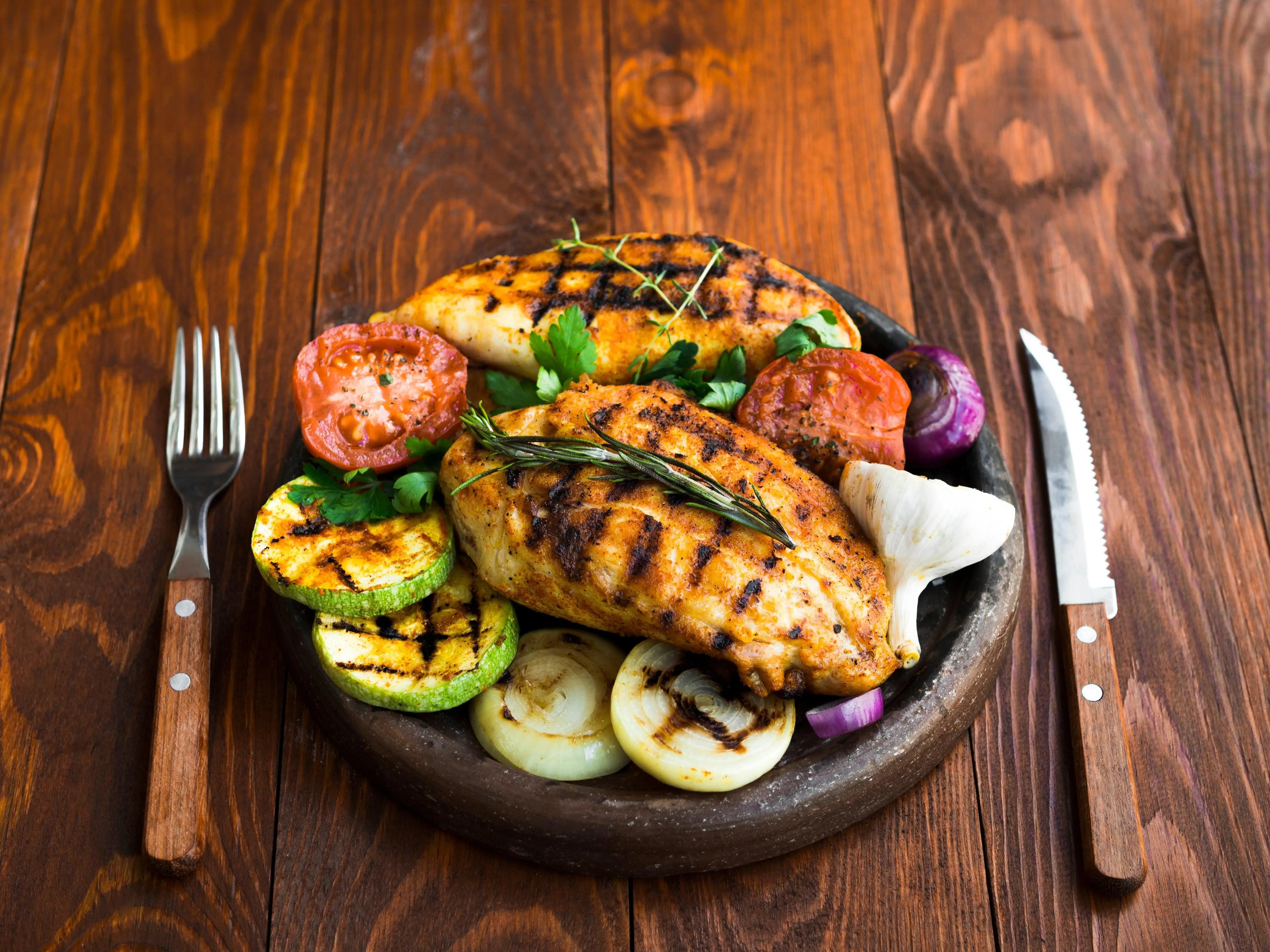 Grilled chicken breast with zucchini, tomatoes, onions, and rosemary on a rustic plate