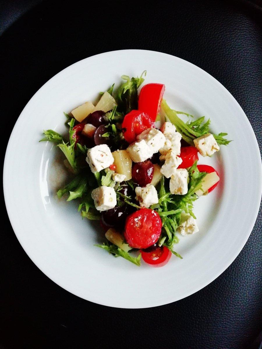 Fresh salad with feta, cherry tomatoes, olives, and greens on white plate