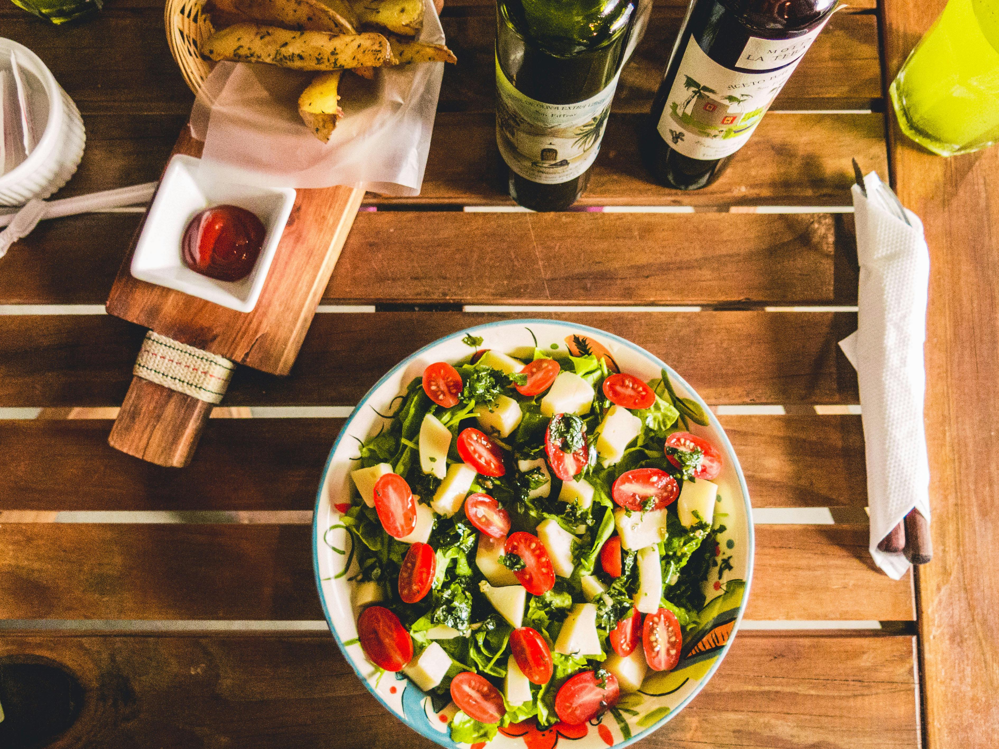 Fresh salad with cherry tomatoes, cheese, and greens on wooden table with olive oil and vinegar bottles