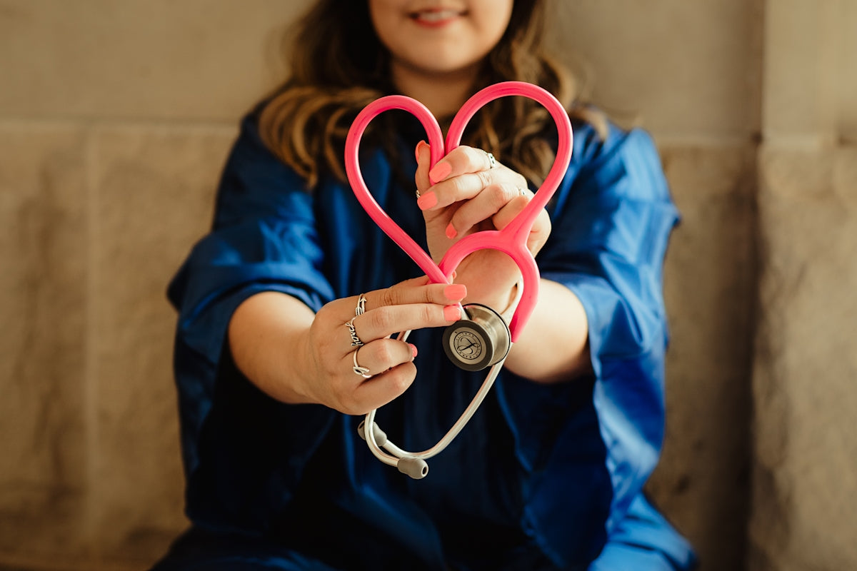 Nurse in blue scrubs holding pink stethoscope shaped into heart, symbolizing healthcare and compassion