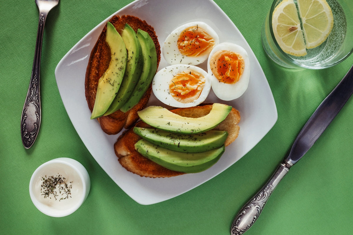 Avocado toast with hard-boiled eggs, herbs, and lemon water on green tablecloth