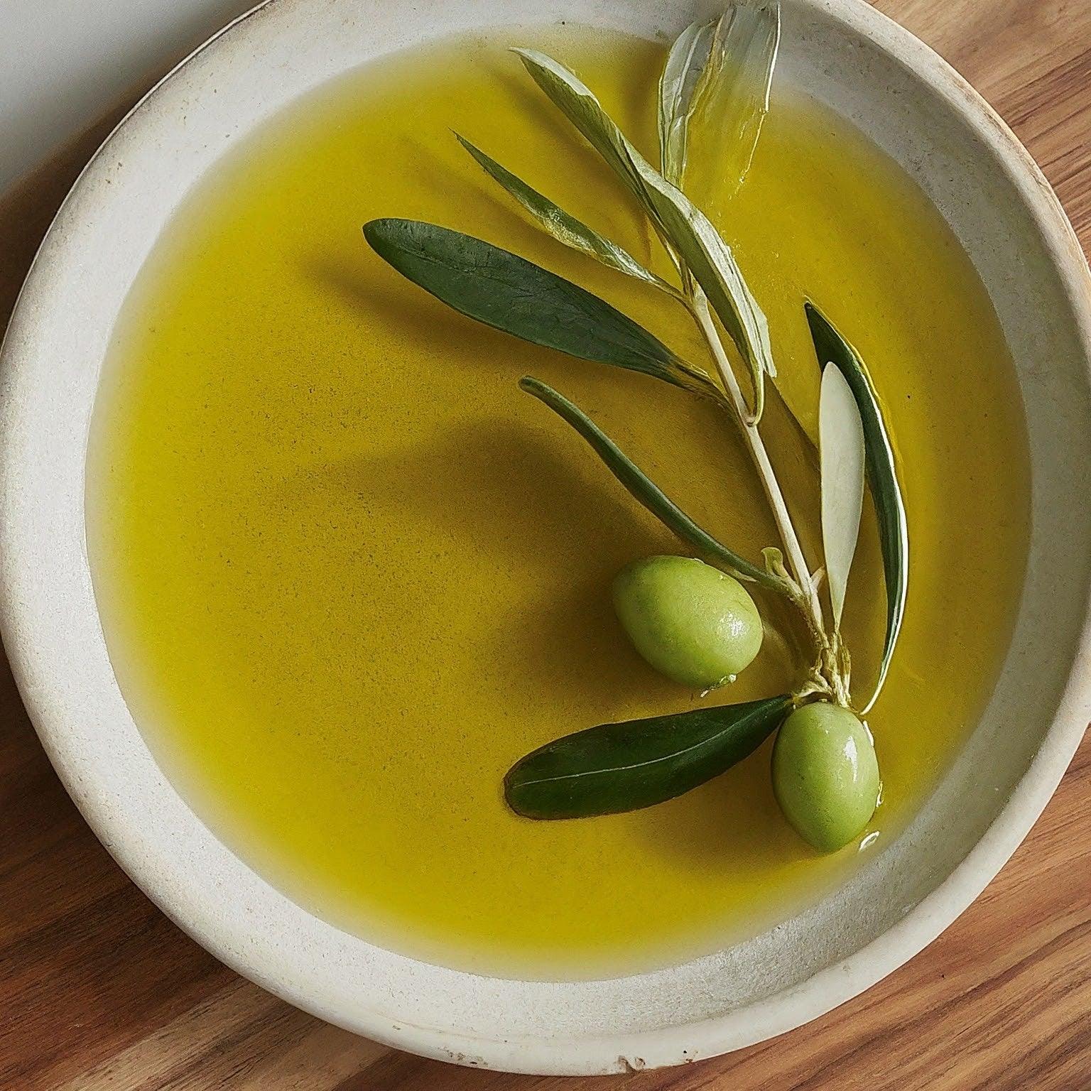 Premium olive oil in ceramic bowl with fresh olive branch and green olives, showcasing artisanal quality