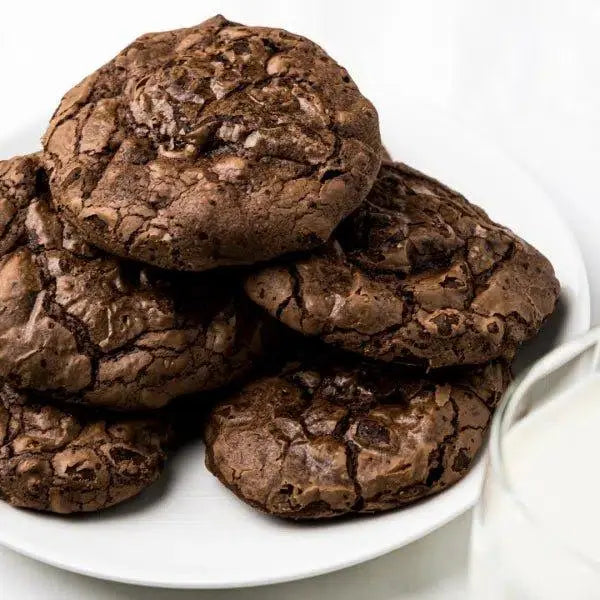 Rich chocolate cookies with cracked tops, served on white plate beside glass of milk