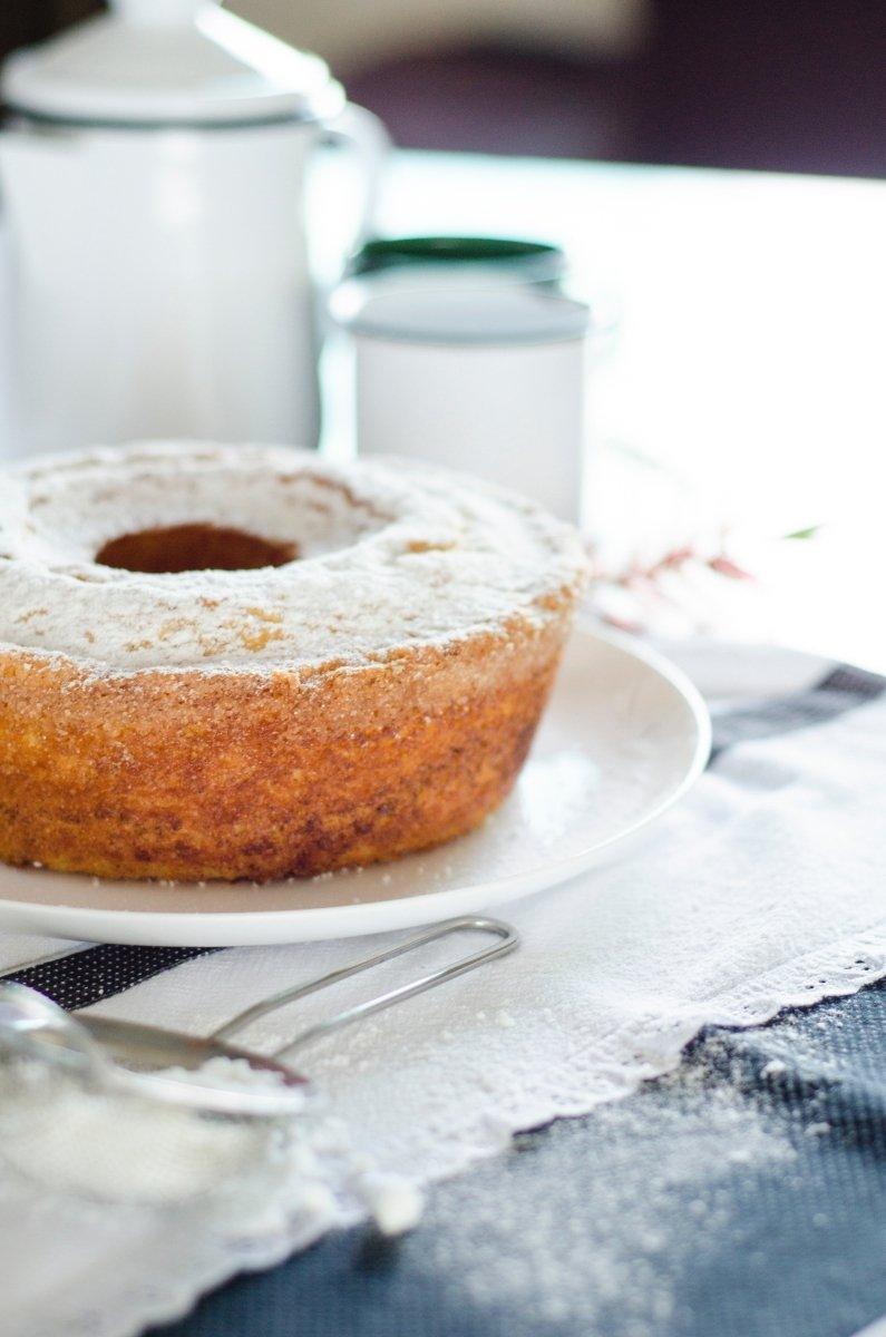 Golden bundt cake dusted with powdered sugar on white plate, rustic table setting