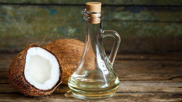 Coconut oil in glass bottle beside fresh coconut halves on rustic wood