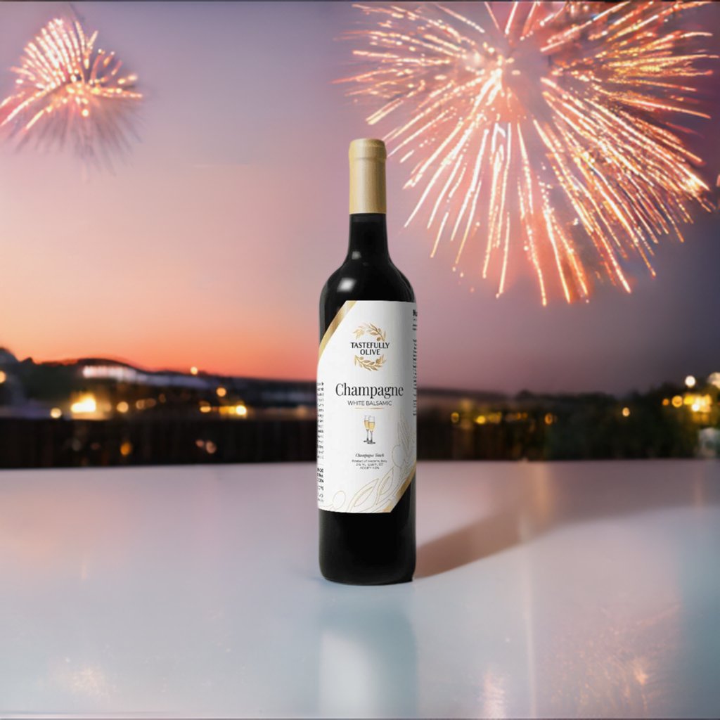 A bottle of Tastefully Olive’s Champagne White Balsamic Vinegar is placed on a table, with fireworks illuminating the Mediterranean sky in the background.