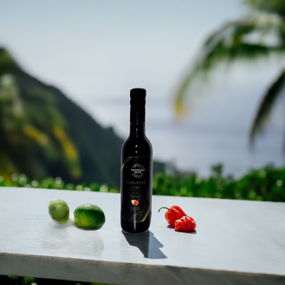A bottle of Tastefully Olive's Lime Habanero Infused Olive Oil is placed on a white table outdoors, flanked by two limes on the left and two habanero peppers on the right, with a scenic view in the background.