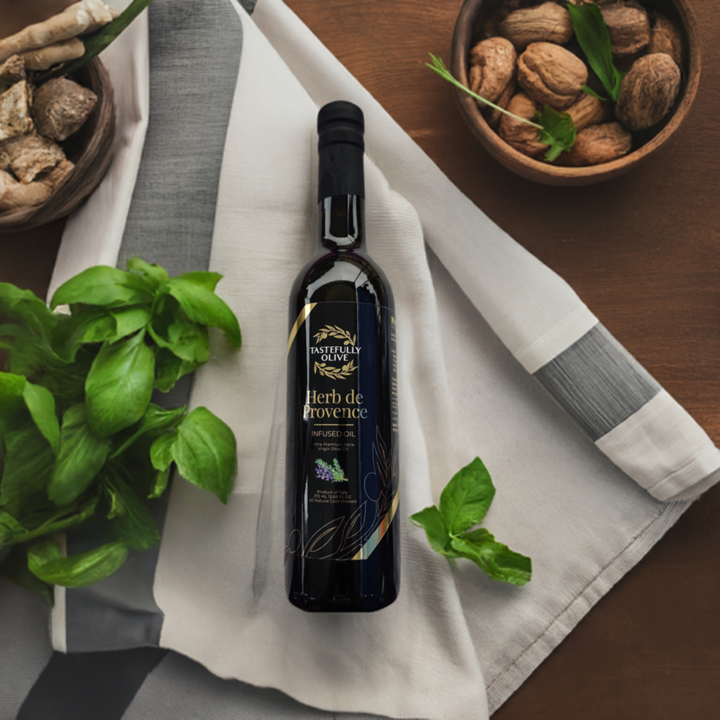 A dark bottle of Tastefully Olive's Herb de Provence sits on a white and gray striped cloth, surrounded by fresh basil leaves and bowls of nuts on a wooden surface.