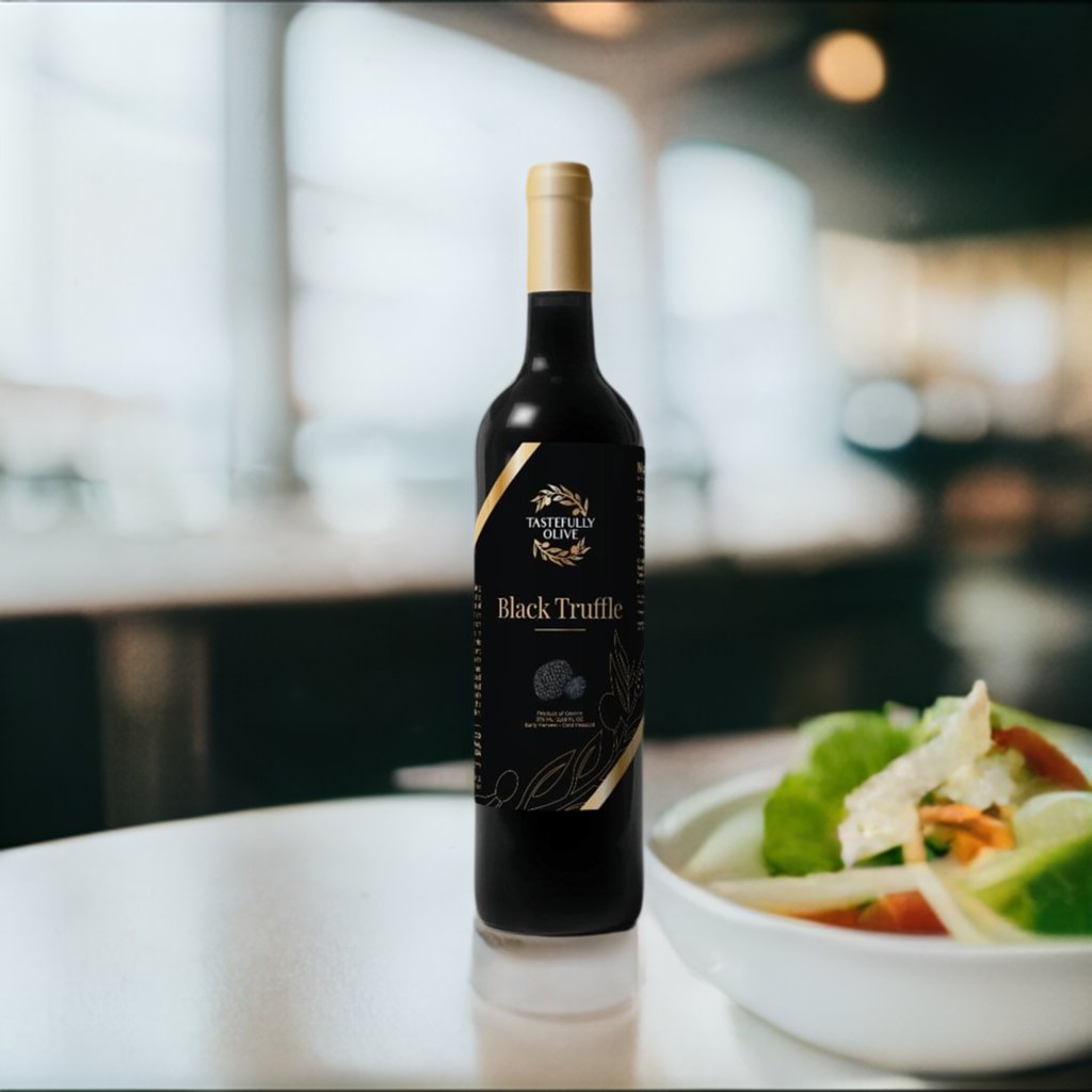 A bottle of "Tastefully Olive Black Truffle Olive Oil" sits on a table next to a fresh salad, complemented by a drizzle of the rich oil, in a bright, blurred dining setting.