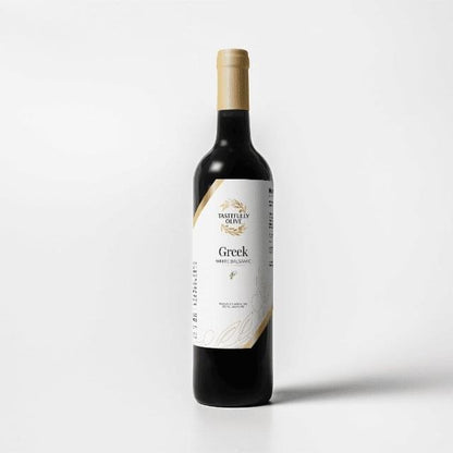 A bottle of Tastefully Olive Greek Seasoning White Balsamic Vinegar with a gold cap and white label stands against a plain white background.