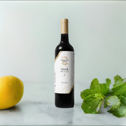 A bottle of Tastefully Olive Greek Seasoning White Balsamic Vinegar stands on a white marble surface next to a lemon, fresh mint leaves, and a versatile balsamic dressing.