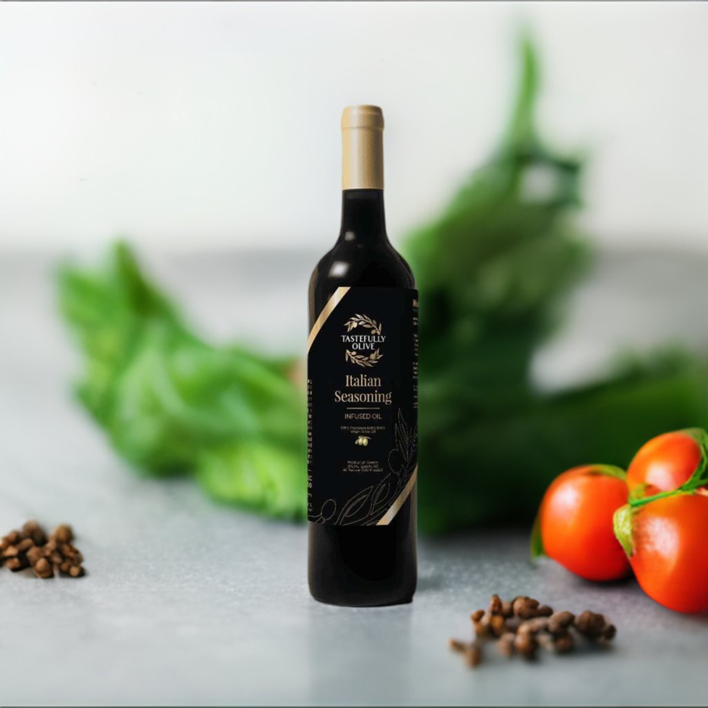 A bottle of Tastefully Olive's Italian Seasoning Infused Olive Oil stands on a countertop, accompanied by scattered peppercorns and tomatoes, with green herbs blurred in the background—a testament to endless culinary possibilities.