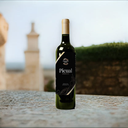A bottle of Tastefully Olive's Picual | Spain stands upright on a textured stone surface, with blurred outdoor elements and an architectural structure visible in the background.